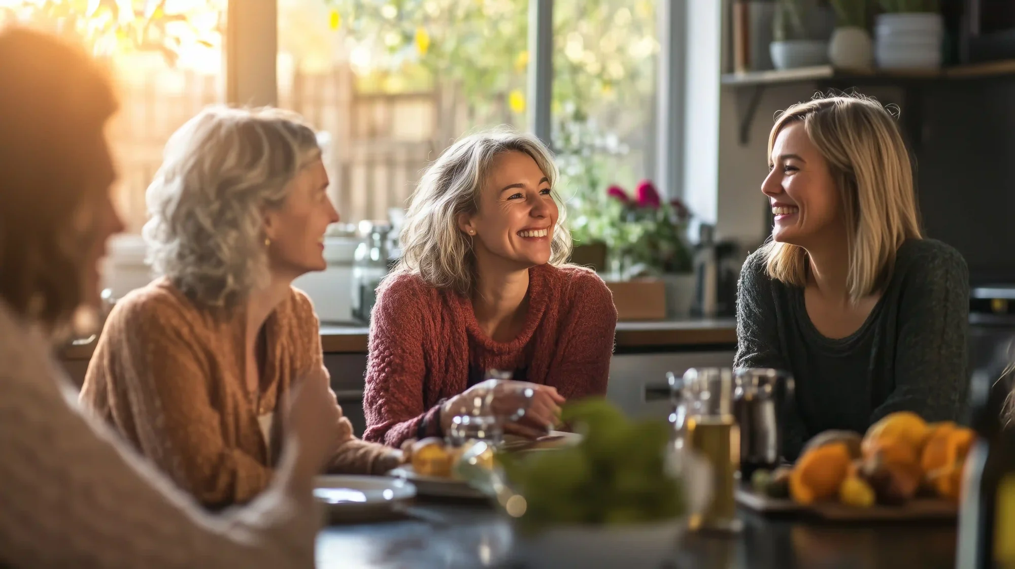 Vier Frauen sitzen zusammen an einem gedeckten Tisch. Sie sind in eine vertraute Unterhaltung vertieft.