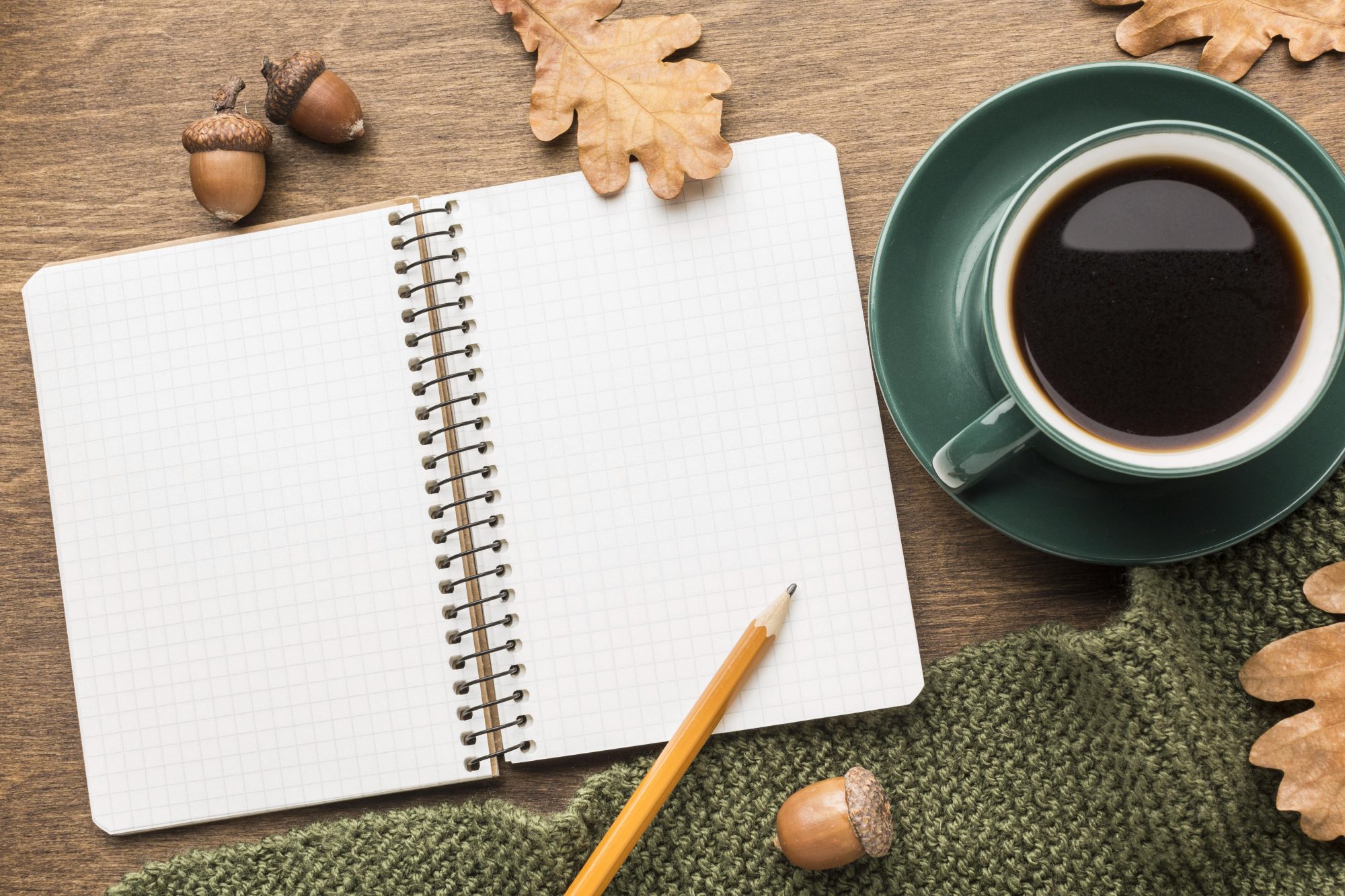 Eine Tasse, ein Schreibblock und ein Bleistift auf einem Tisch mit herbstlicher Dekoration