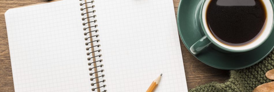 Eine Tasse, ein Schreibblock und ein Bleistift auf einem Tisch mit herbstlicher Dekoration